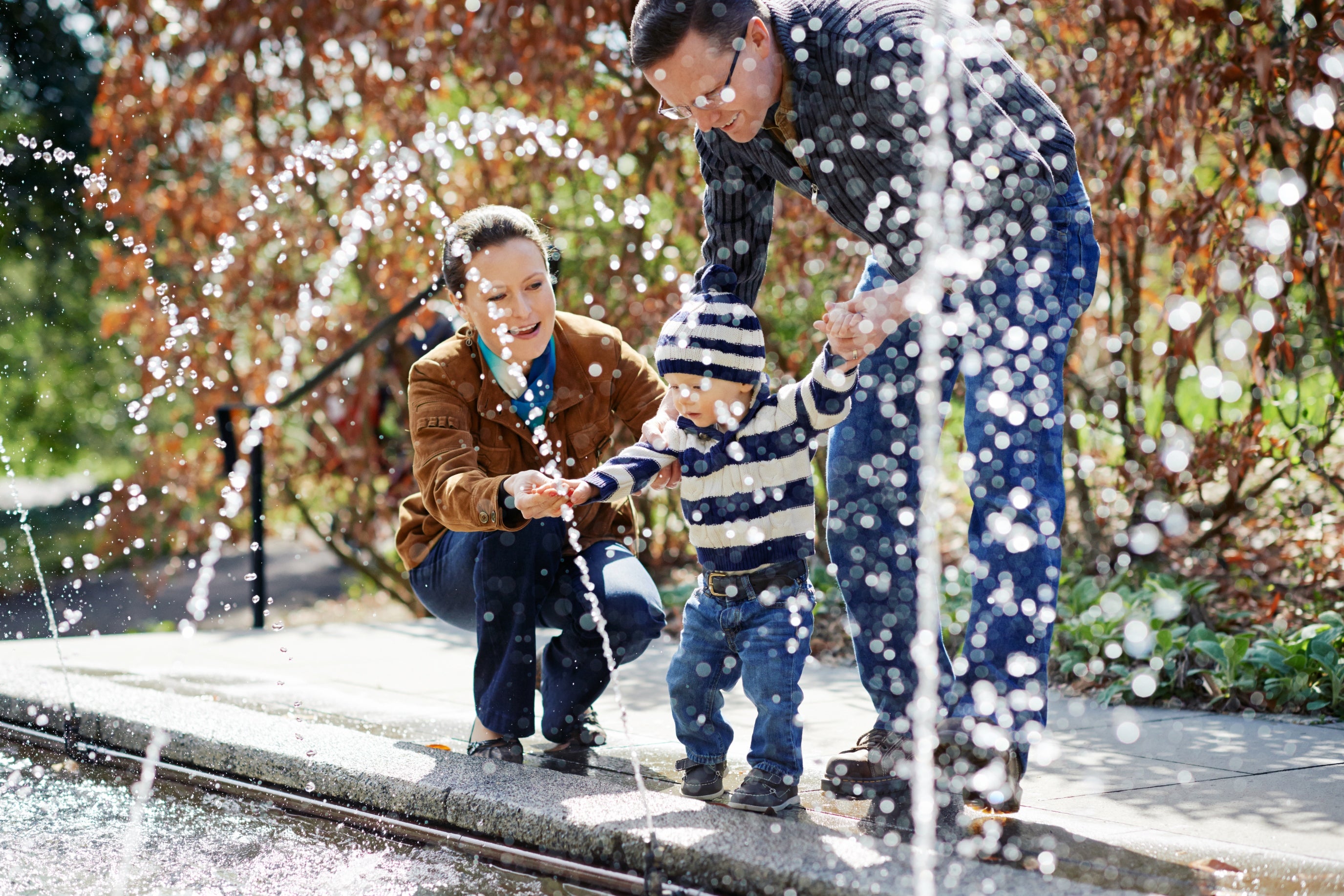 Members.jpg a man and a woman holding an infant in front of the fountain