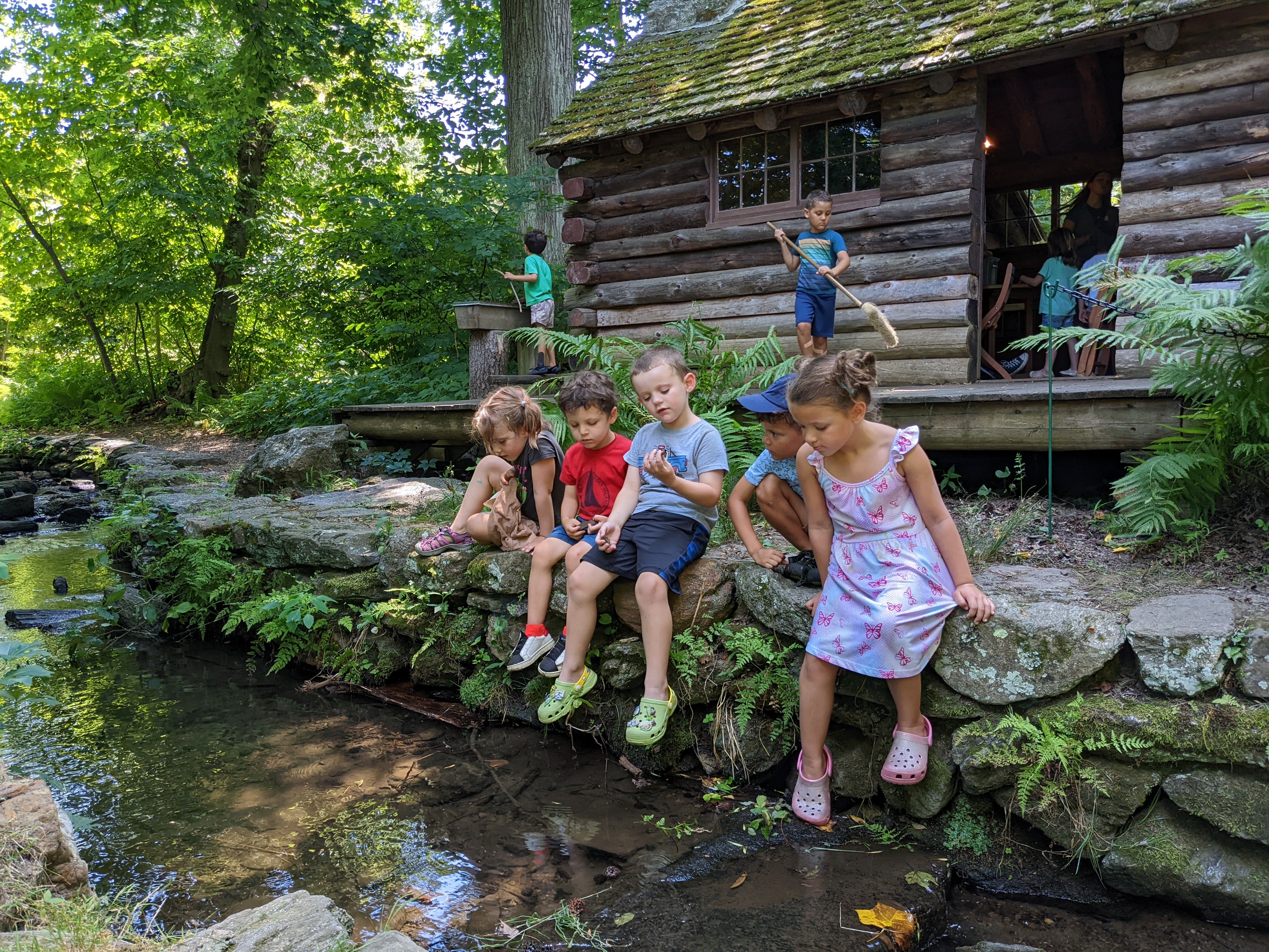 summer camp.jpg A group of children sit on a rock wall looking into a creek.