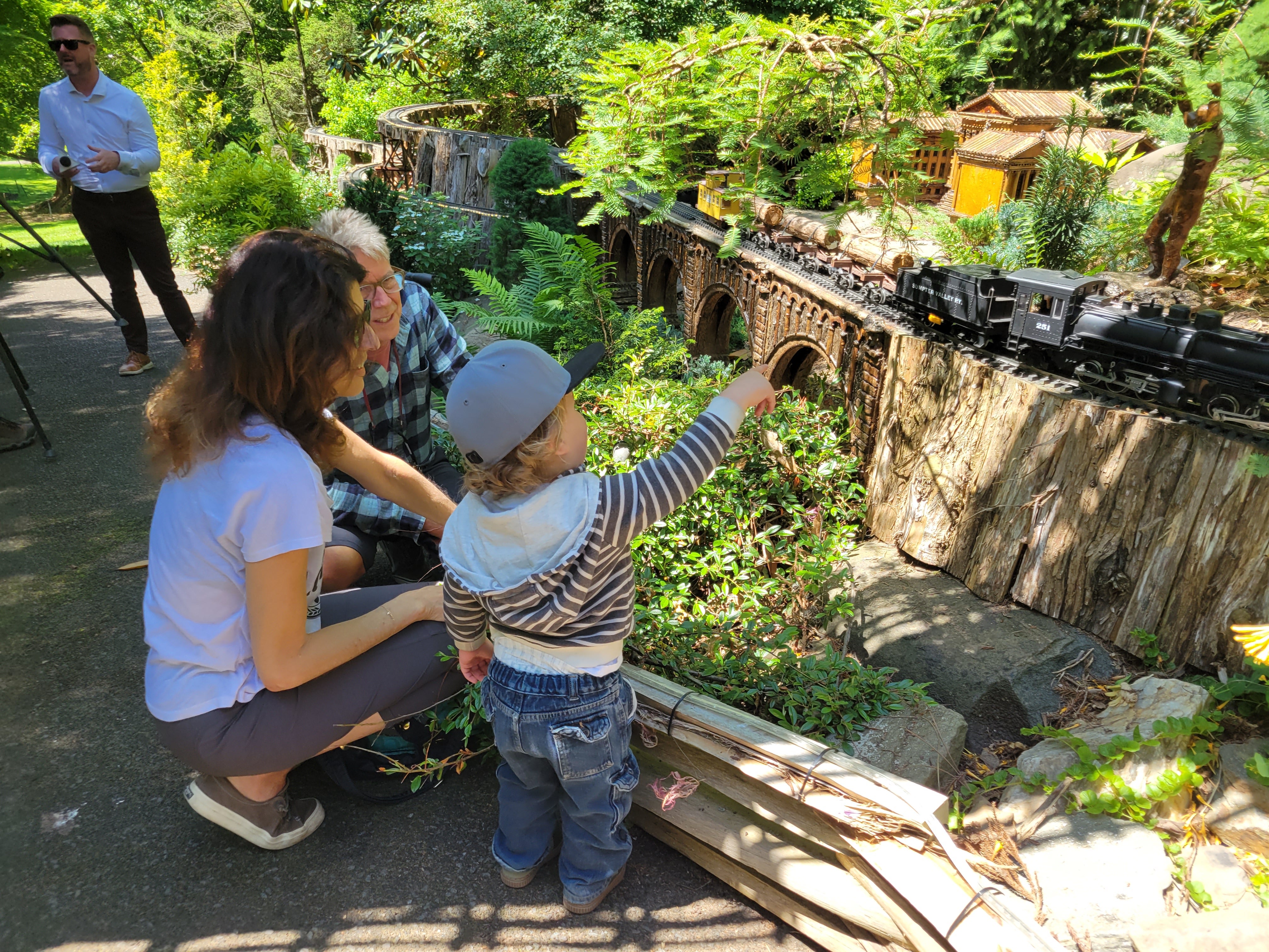 A man, woman, and child look at a miniature train on an outdoor track.