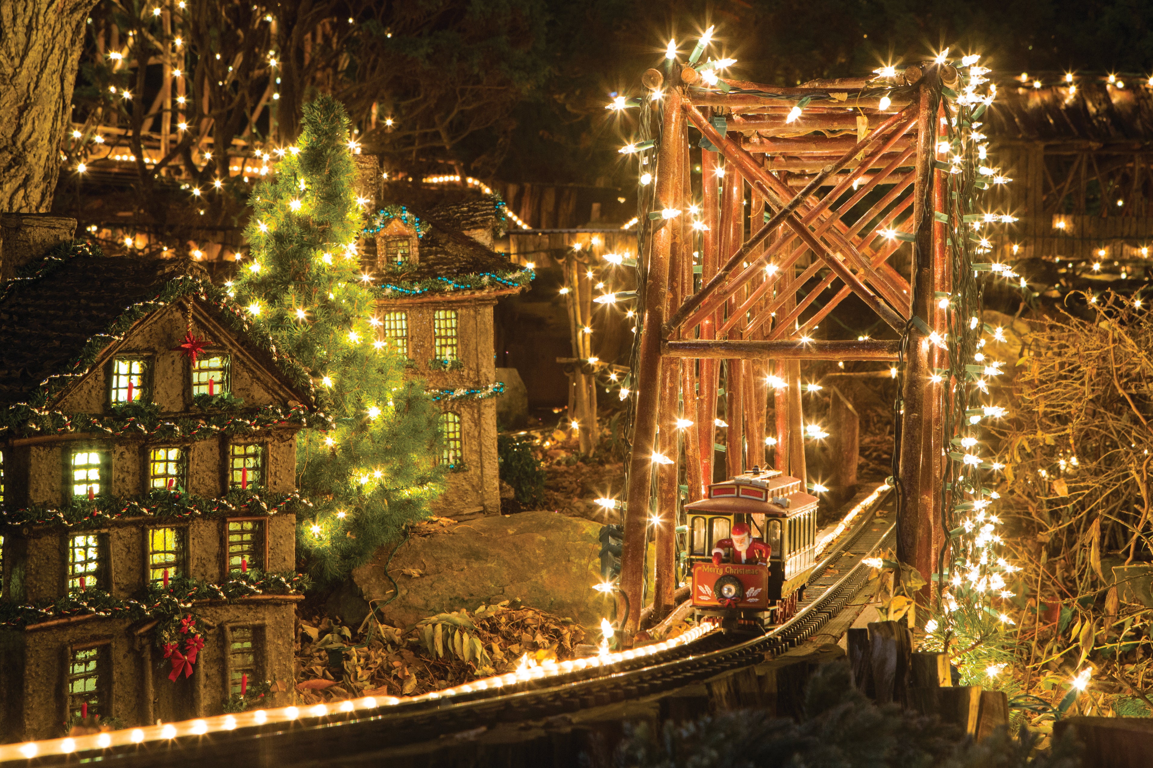 A miniature train display with a trestle bridge, a train with Santa, and lots of holiday lights.