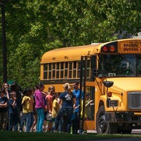 A group of young students wait in a line to board a school bus. 
