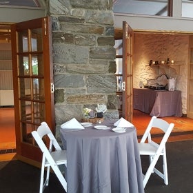 A wedding sweetheart table with a grey tablecloth and place settings in a stone building.