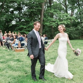 A bride and groom walk smiling while their guests are in the background. 
