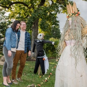 A man and woman laughing while looking at Halloween scarecrows.