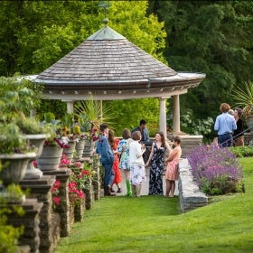 A group of people in informal attire next to a gazebo in a blooming rose garden.