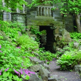 A grotto surrounded by pink flowers and green foliage.