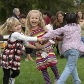 Three young girls hold hands in a circle, smiling and dancing. 