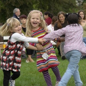 Three young girls hold hands in a circle, smiling and dancing.