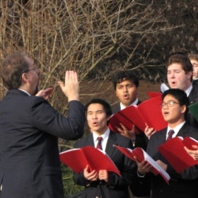 A choir conductor leads a group of college students in song. 