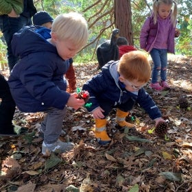A group of small children hold decorated holiday pinecones outdoors. 