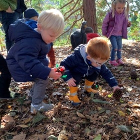 A group of small children hold decorated holiday pinecones outdoors.