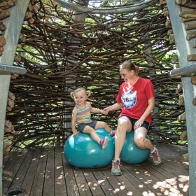 A mother and daughter sit inside a large, prefabricated birds nest with bright blue eggs. 