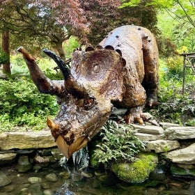 A fabricated triceratops made of natural materials and set in a green landscape. 