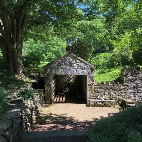 A stone spring house surrounded by trees and green foliage. 