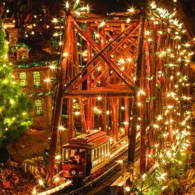 Model train trolley car going over a bridge covered in white lights