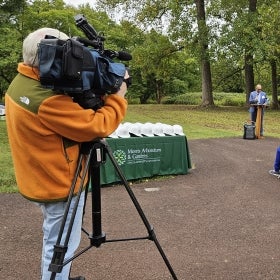 TV camera man stands in front of table with white hard hats on it