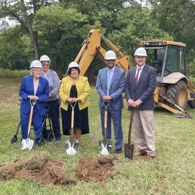 Five men and women in white hardhats holding shovels