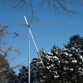A tall kinetic metal sculpture set against a background of winter evergreens dusted with snow and a blue sky.