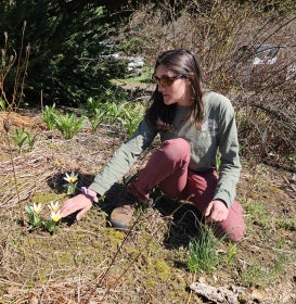 A woman with dark hair and sunglasses squats down near yellow tulips