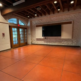 An empty classroom with French doors leading outside and a large TV on the wall. 