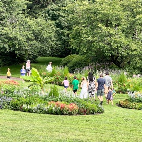 People walk through paisley-shaped flower beds in bloom in a public garden on a sunny day. 