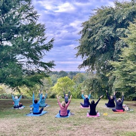A group of people sit on yoga mats in an outdoor space doing yoga.