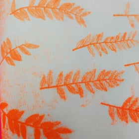 A white sheet of paper with many orange prints of a fern frond all over it. 
