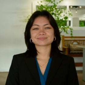 A headshot of a young woman in a black blazer and bright blue shirt. 
