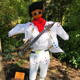 A scarecrow dressed to look like Elvis Presley in a white jumpsuit and holding a guitar
