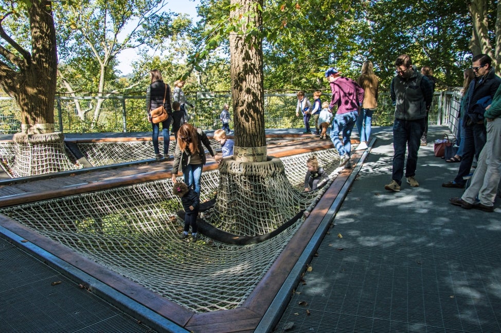 Families climbing through an elevated hammock-like net in the trees.