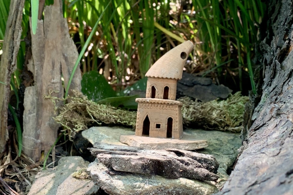 A small, ceramic fairy house in the woods. 