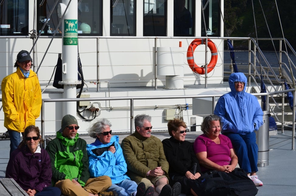 A group of people sit on a boat dressed in jackets and smiling. 