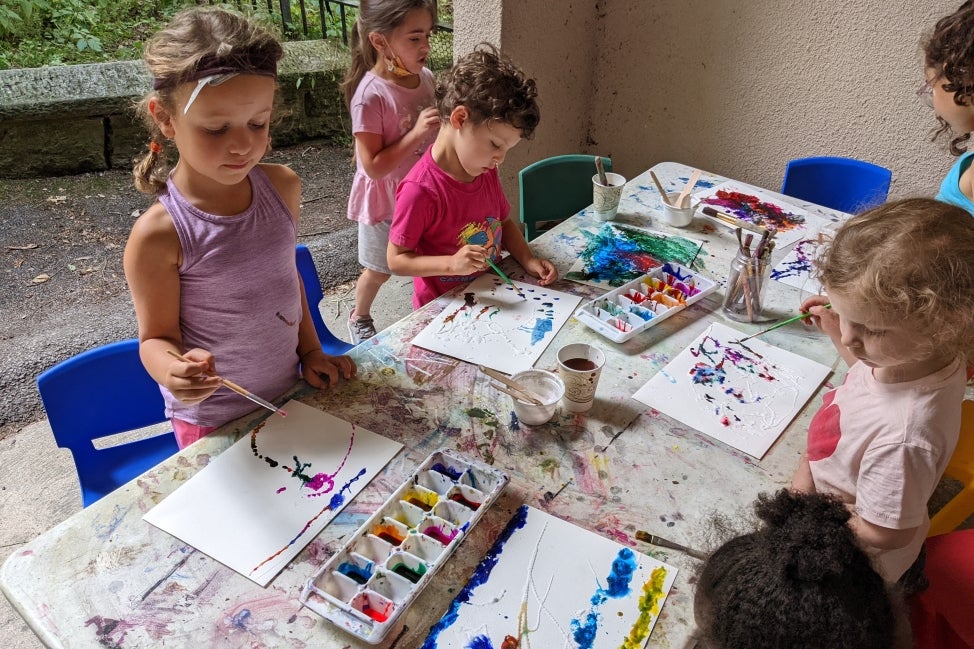 A group of young children sit at a table and paint. 