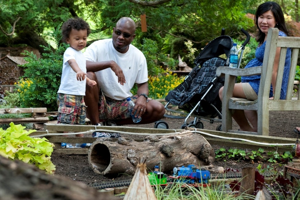 A family watches miniature model trains on an outdoor track.