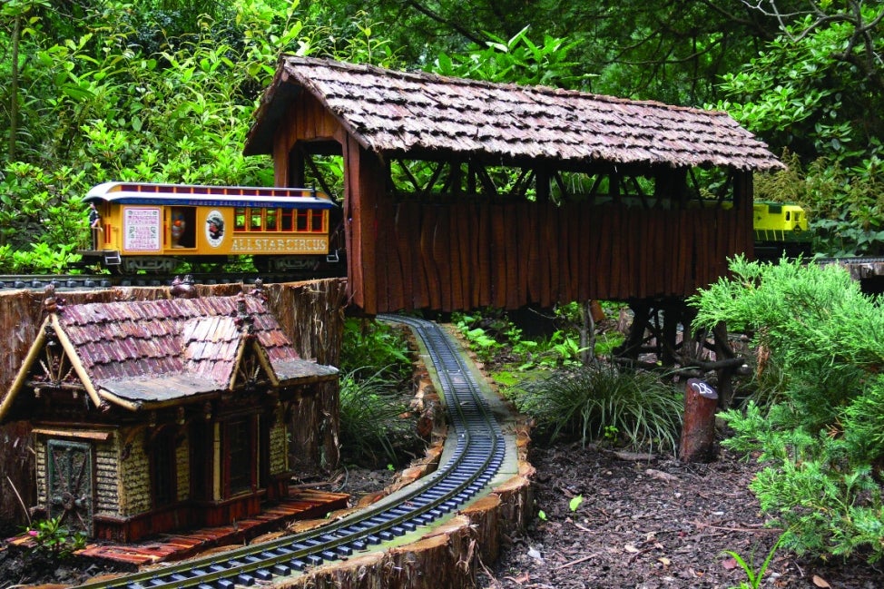 A miniature train runs through a miniature covered bridge.