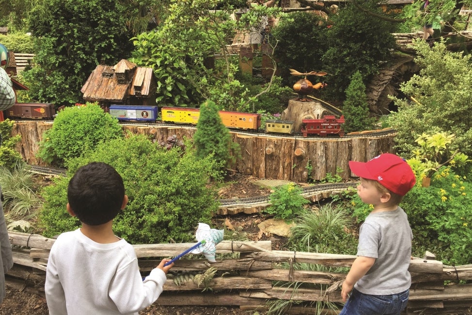 Two children watch a model train ride through a miniature track.