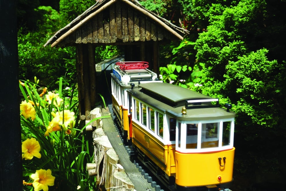 A model trolley train rides through a miniature covered bridge.