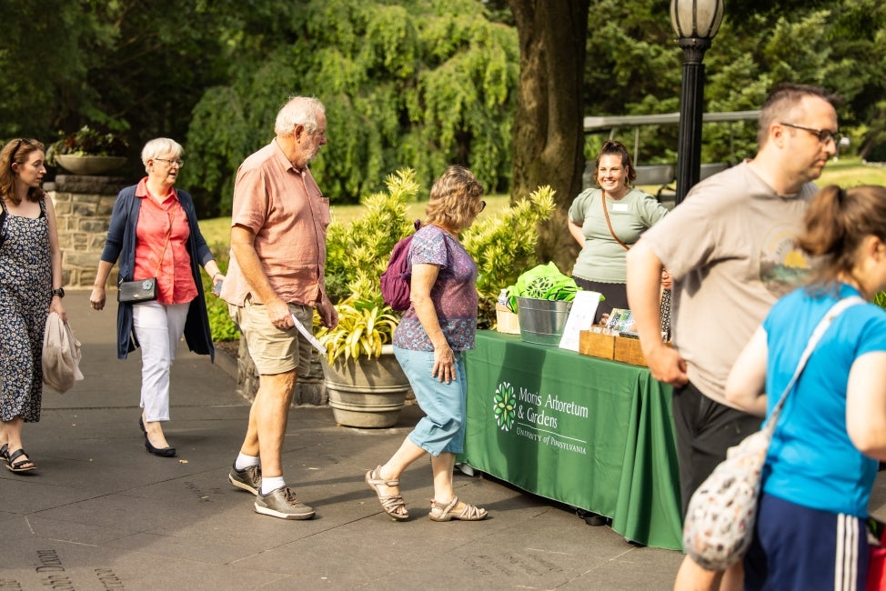 A line of people standing in front of a Morris Arboretum & Gardens registration table outside. 