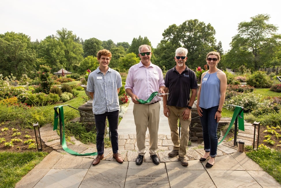 Four people posed for the camera in front of a public garden in bloom. 