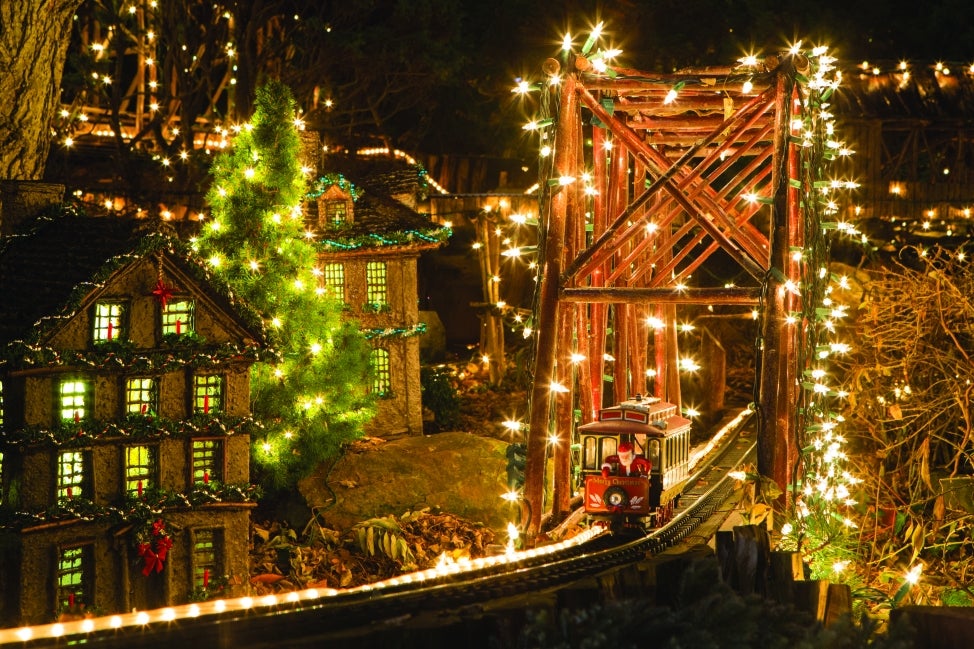 A miniature train display decorated in holiday lights with a mini Santa riding on a train.