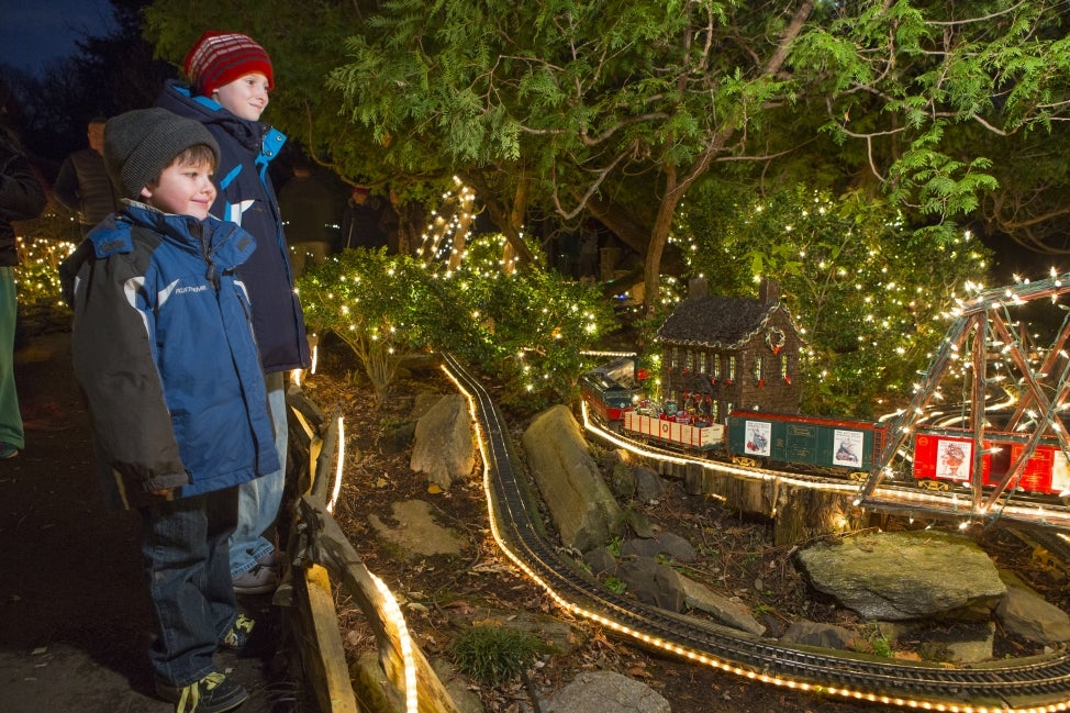 Two young boys smile while waiting a miniature train display decorated for the holidays.