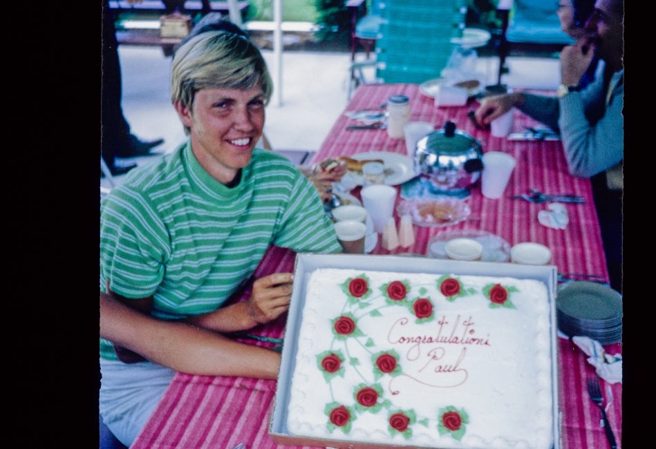 A young man sits with a cake that says, "Congratulations Paul."