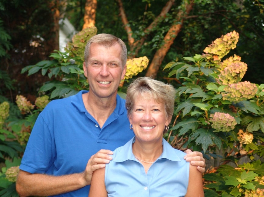 A man and woman pose in front of a flowering shrub. 