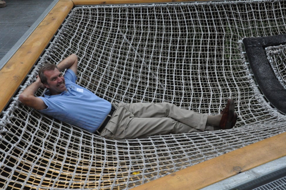 A man reclines in a netted hammock with his hands behind his head. 