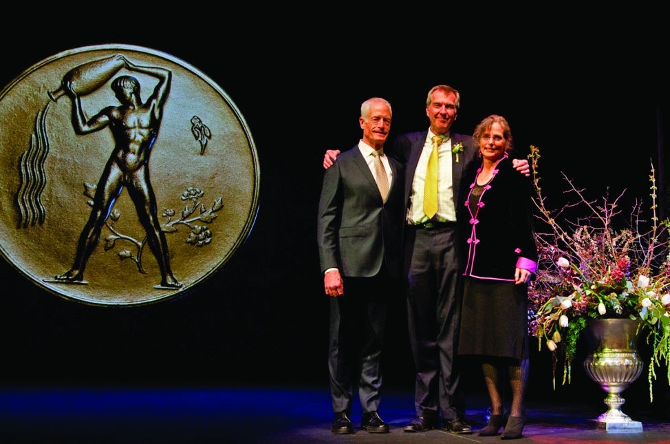 Two men and woman pose on stage during an awards ceremony. 