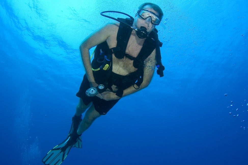 A man scuba diving in bright blue water. 