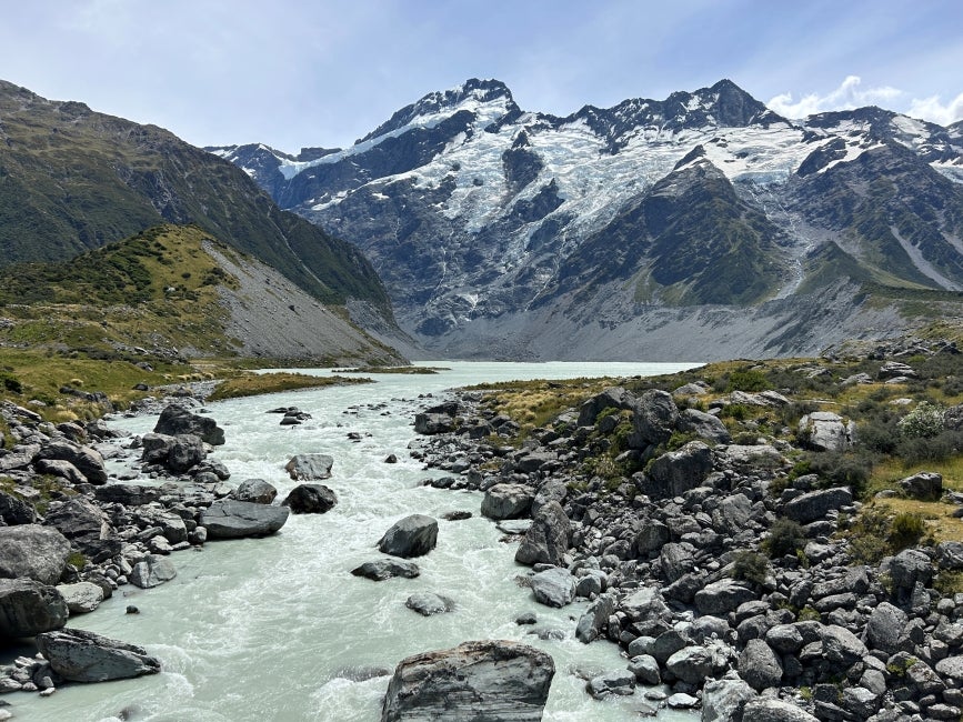 A glacial body of water winding through a rocky landscape with mountains in the background. 