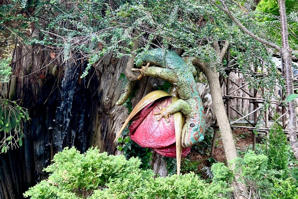 A large sculpture of a gecko next a small waterfall and surrounded by plants.