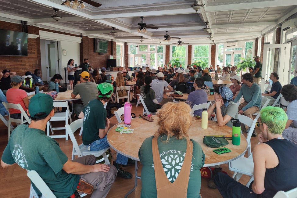 A large group of interns from various Philadelphia-area public gardens sit at round table while listening to a speaker. 