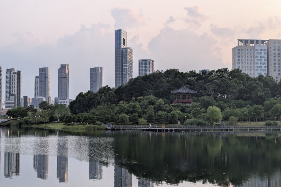 A city park in Sejong, South Korea with a waterway in the foreground and greenery and buildings in the background. 